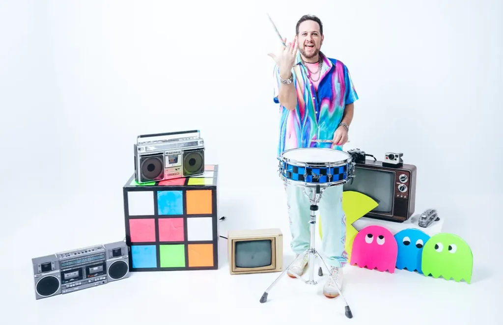 cary g twarling a drumstick behind snare drum surrounded by 80s props