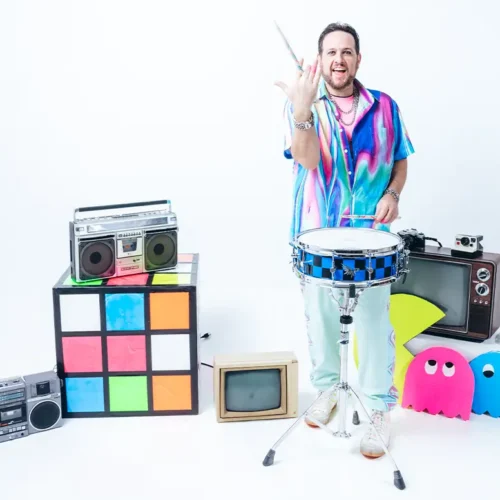 cary g twarling a drumstick behind snare drum surrounded by 80s props
