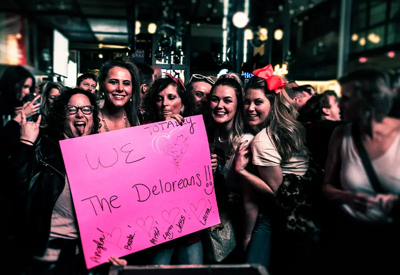 girls holding a pink sign that says "we love the deloreans"