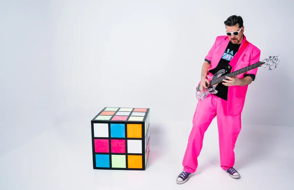 jess mcfly playing a clear bass next to a giant rubix cube