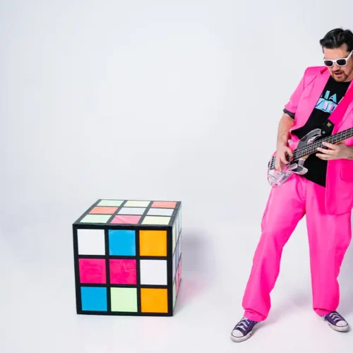 jess mcfly playing a clear bass next to a giant rubix cube