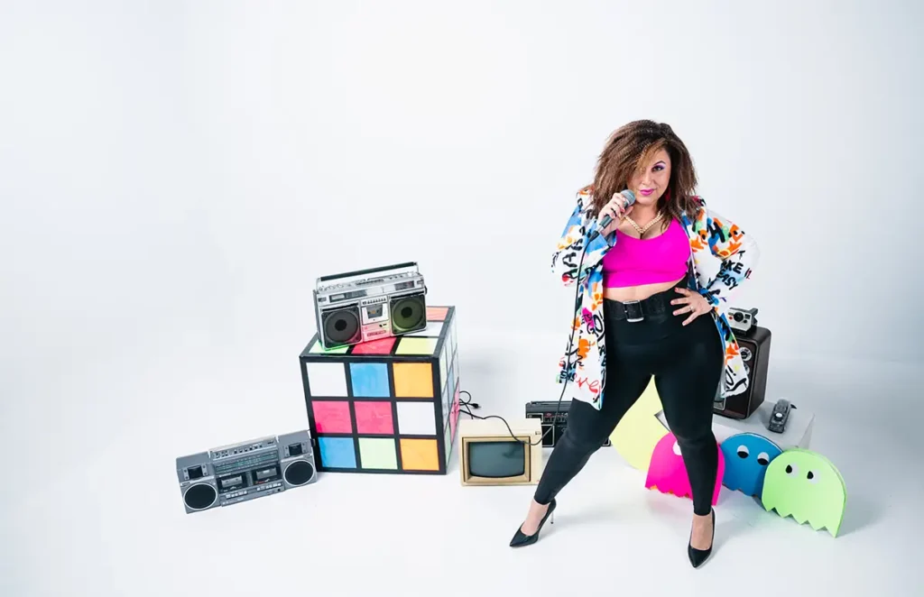 rianna delorans holding a microphone surrounded by 80s props